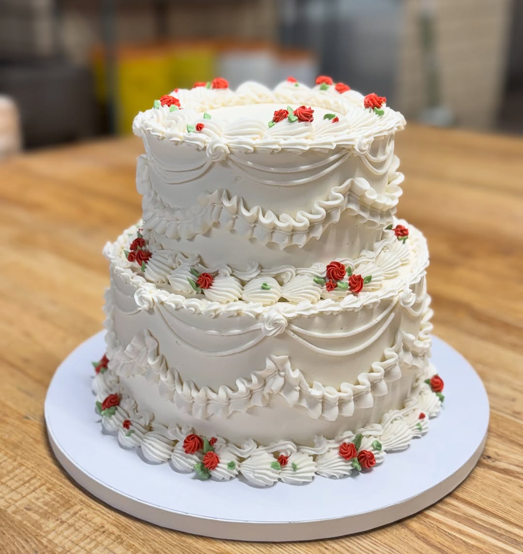 Two-tier white cake with red buttercream roses on the bench
