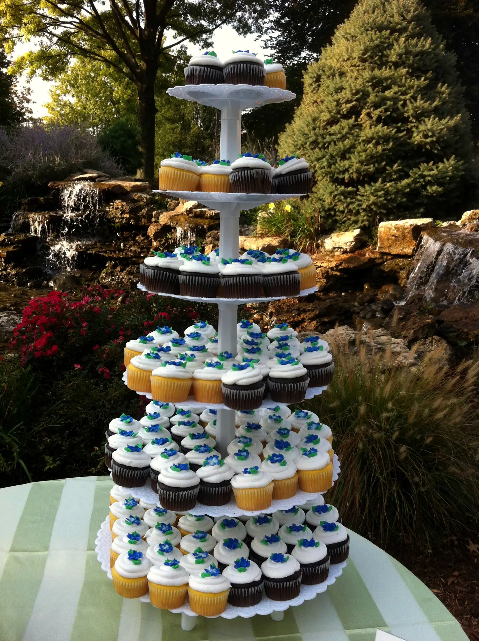 Five-tier stand of iced cupcakes set out at an outdoor party