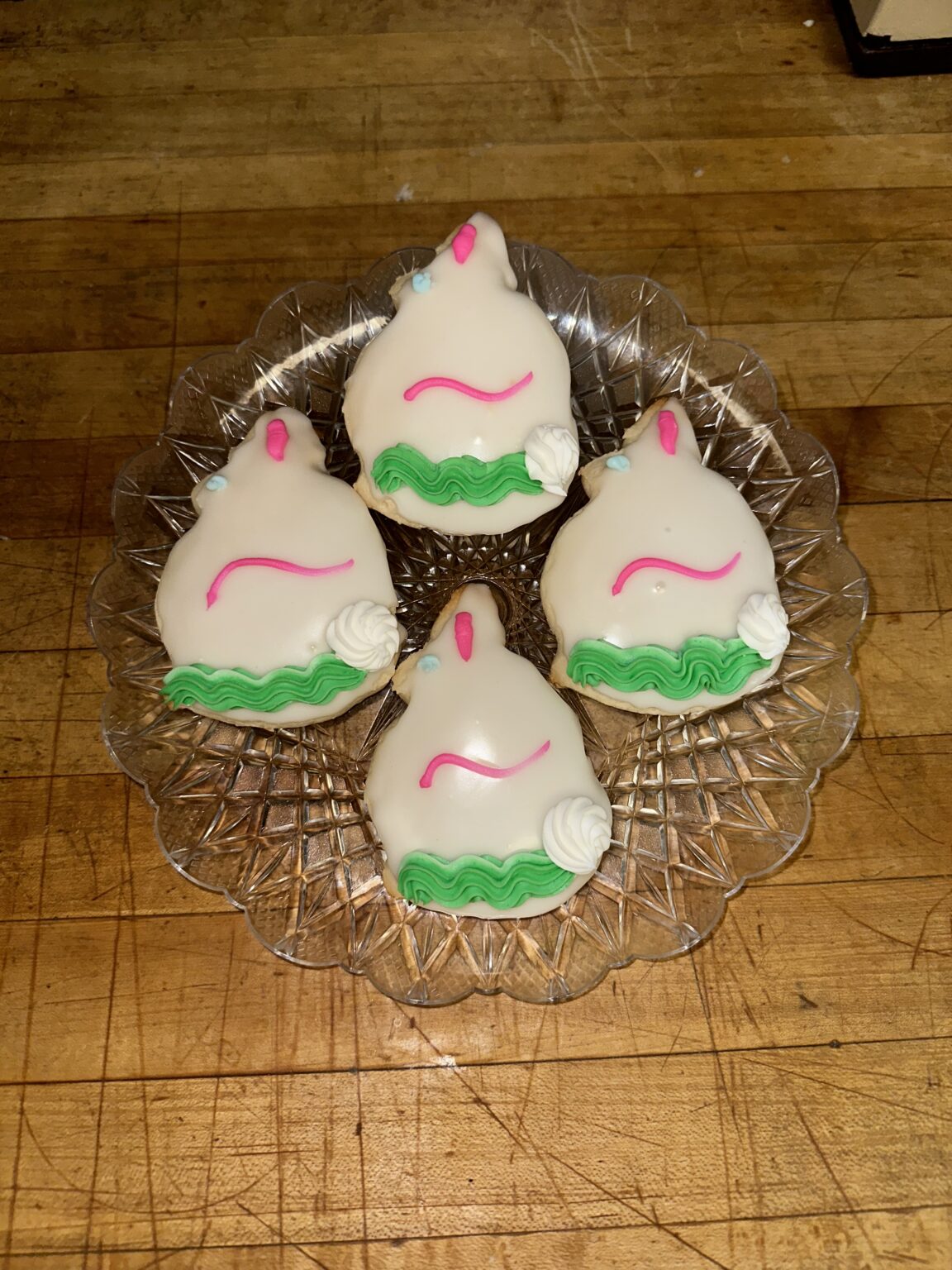Four white-glazed Easter cookies with pink piping, green ruffle icing and icing roses on a pressed-glass plate
