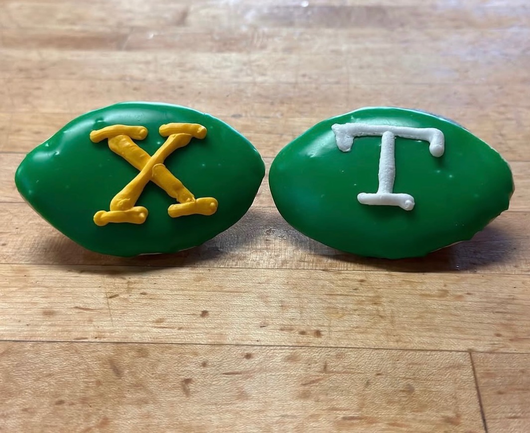 Two green football-shaped iced cookies lettered X and T