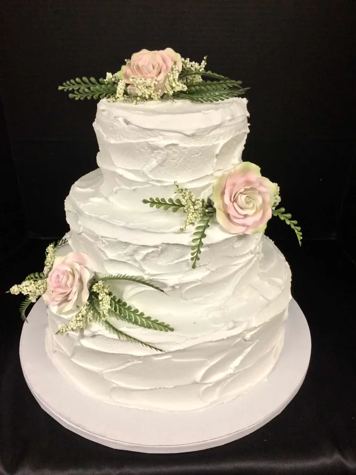 Three-tier white textured wedding cake with pale pink roses