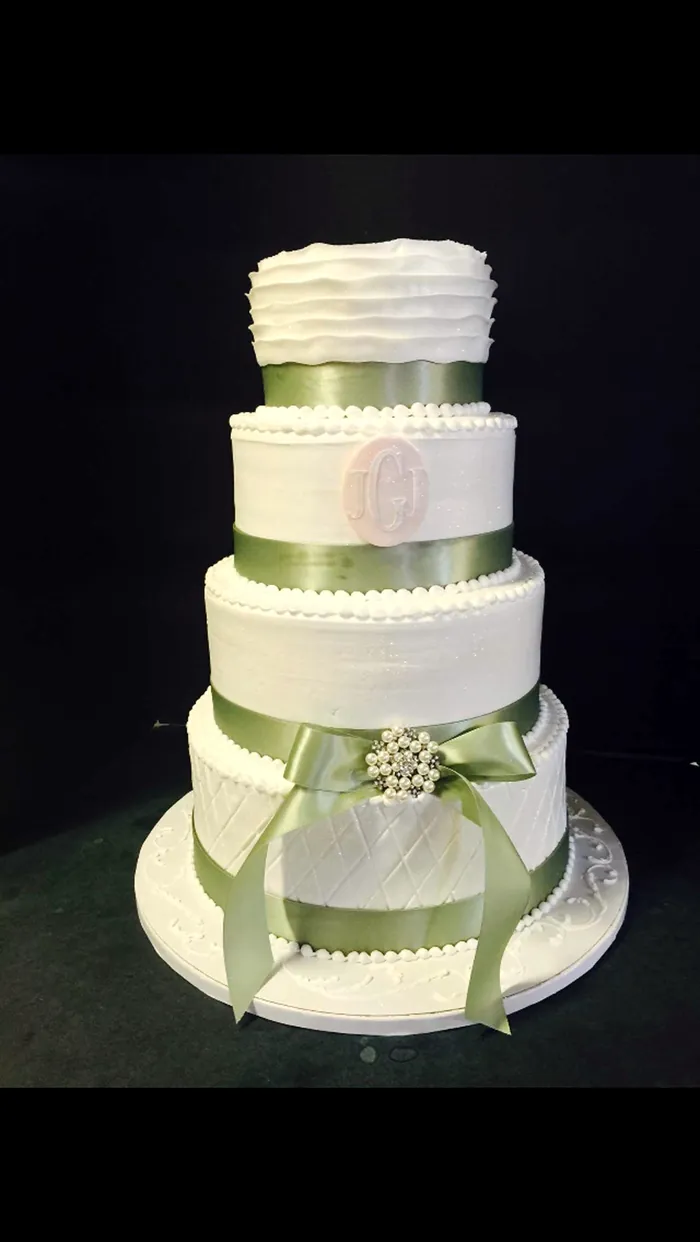 Four-tier buttercream cake with sage ribbon and brooch