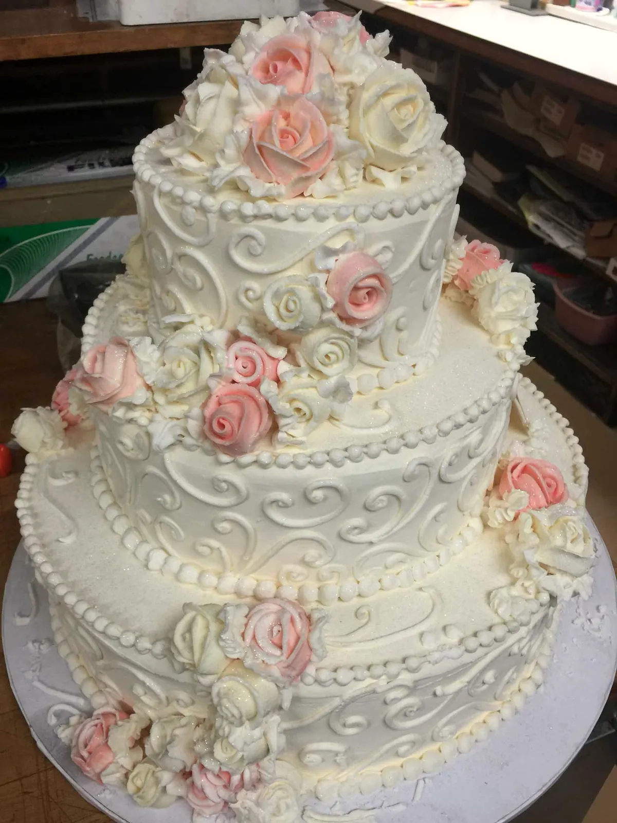 Scrolled buttercream wedding cake with pink and ivory roses